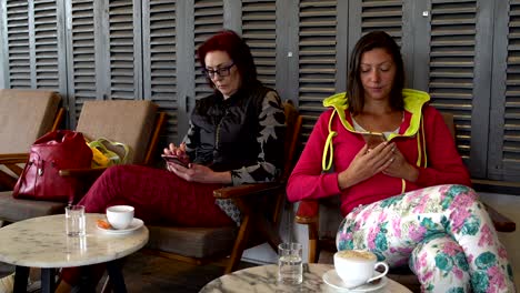 mujeres en una cafetería con teléfonos inteligentes. la chica pone el teléfono en la mesa y bebe café