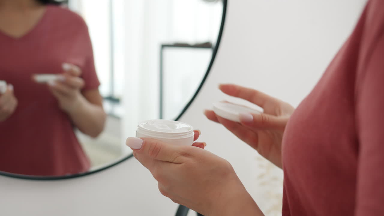 거울 앞 에서 얼굴 크림 을 바르는 여자