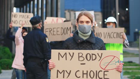 caucasian wearing facial mask holding my body my choice" signboard and looking at camera in a protest against covid 19"