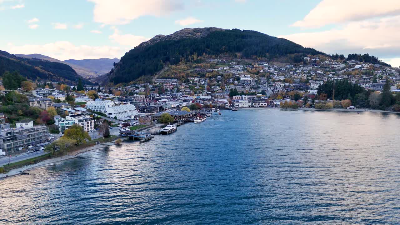 Drone footage captures Queenstown's scenic landscape and Lake Wakatipu under soft daylight, showcasing natural beauty and urban charm