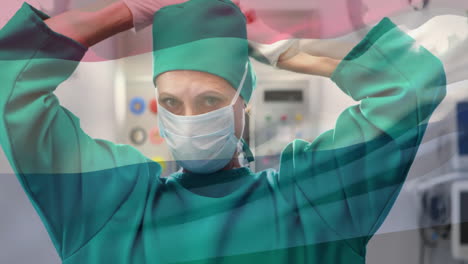 animation of flag of netherlands over caucasian female surgeon wearing face mask