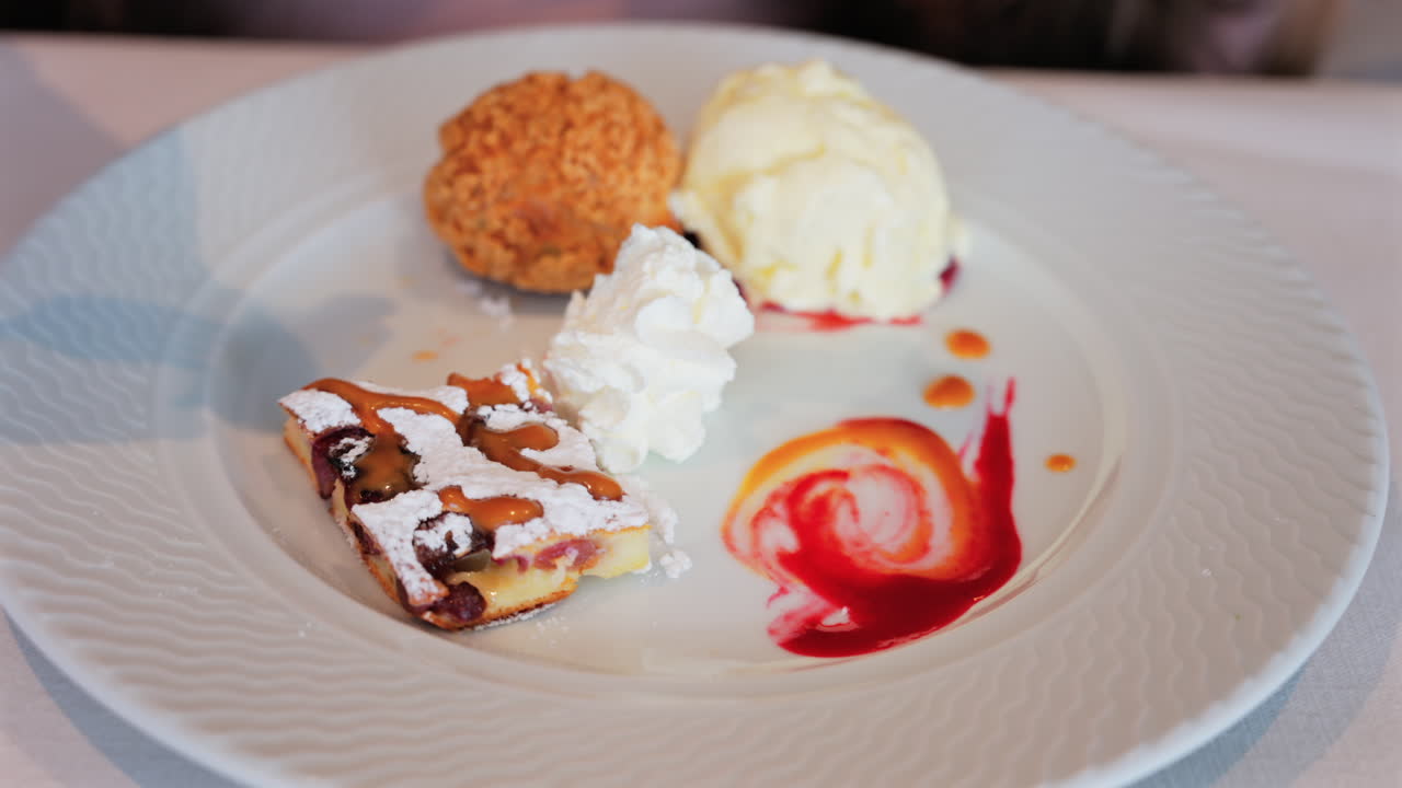 Close up of a woman eating dessert plate with a tart, a cream puff, ice cream, and sauces