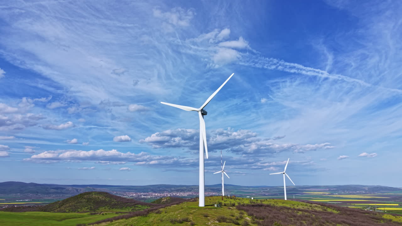 Turbine eoliche si ergono su una collina in un campo verde sotto un cielo blu con nuvole sullo sfondo durante il giorno.