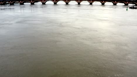 Pont-de-Pierre-bridge-in-Bordeaux-France-with-Garonne-river-on-overcast-day,-Aerial-tilt-up-approach-shot