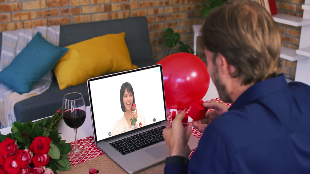 Casal diverso em um encontro de Dia dos Namorados por videochamada, homem mostrando anel para mulher sorrindo na tela do laptop.