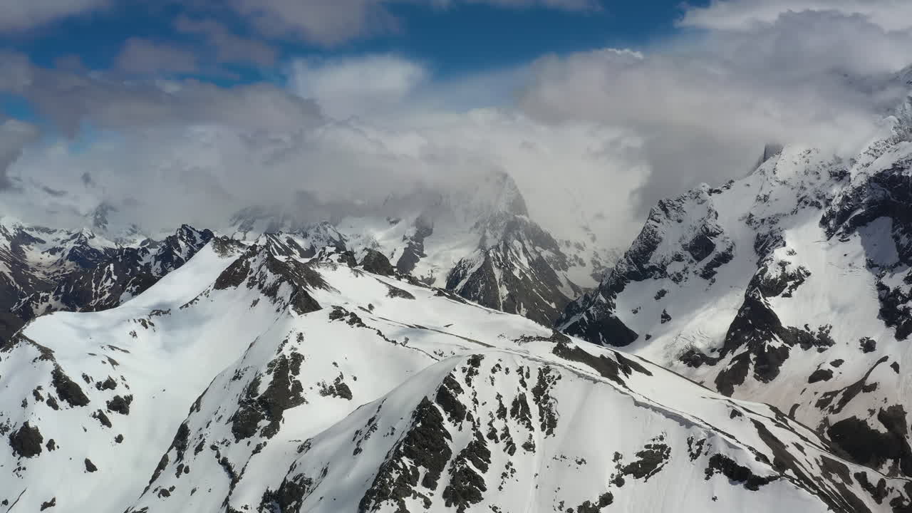 Volo aereo tra le nuvole di montagna sopra splendide vette innevate e ghiacciai.
