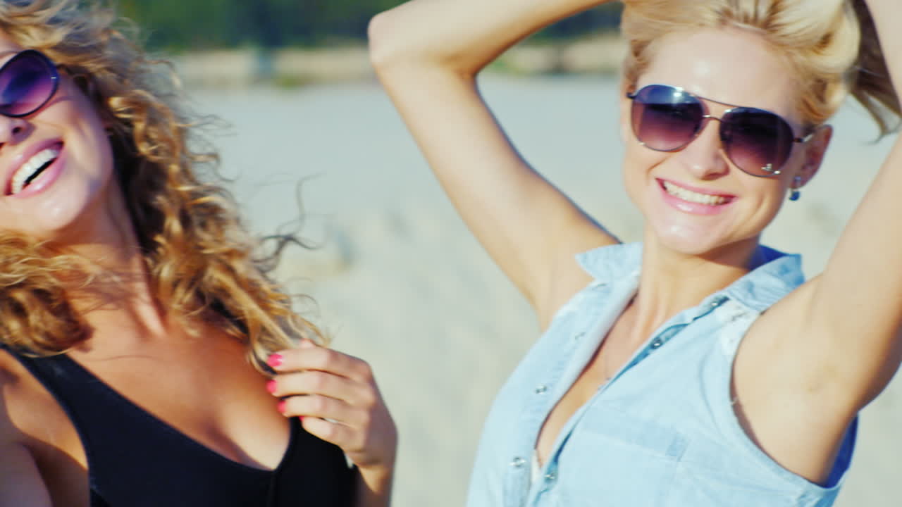 две молодые женщины позируют перед камерой, улыбаясь на пляже в солнечный день
