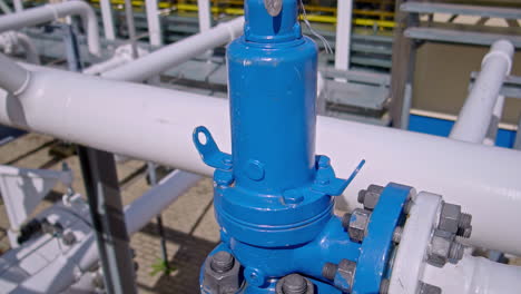 detailed view of a blue industrial gas pressure relief valve mounted on a white pipeline at a facility