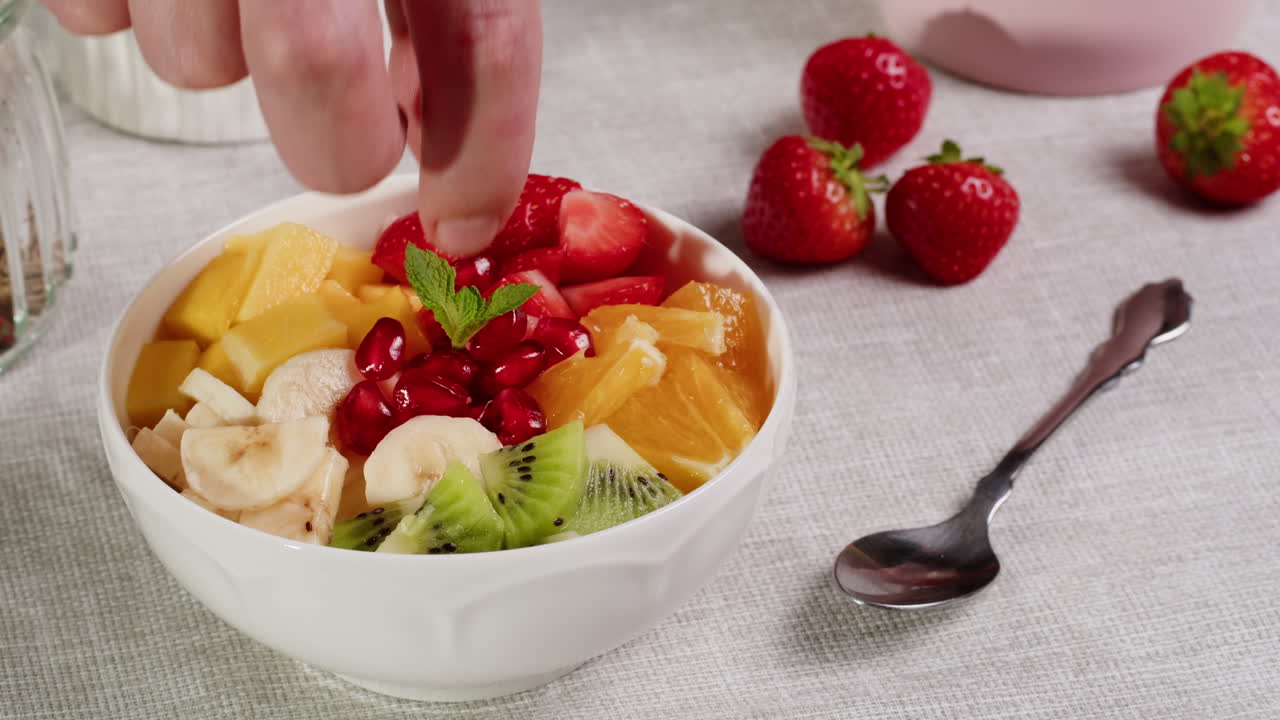 Hand Garnishing a Colorful Fruit Salad Bowl with Fresh Mint