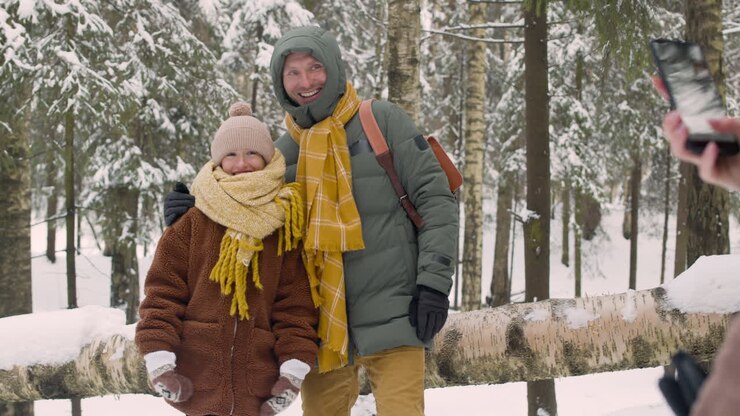 Vue de dos d'une femme photographiant son mari et sa fille dans la forêt enneigée.
