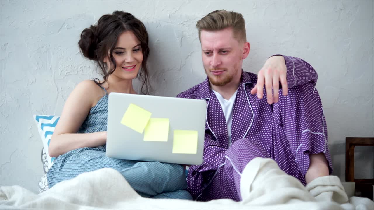 una pareja viendo una computadora portátil en la cama.