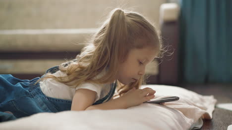 little girl in denim dress plays with mobile phone on floor