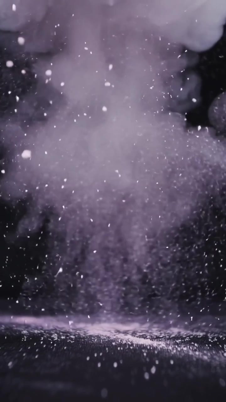 Video verticale: Punto d'impatto in eruzione che invia un denso pennacchio di particelle su una superficie piana, con goccioline.