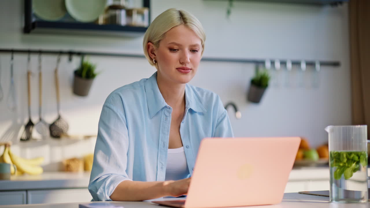 Blond freelancer tjekker smartphone notifikation, mens hun chatter i køkkenet tæt på