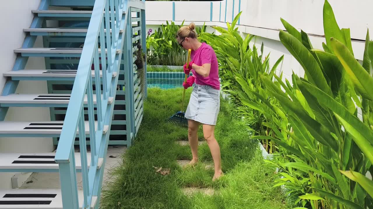 mujer rastrillando hojas en un patio trasero tropical