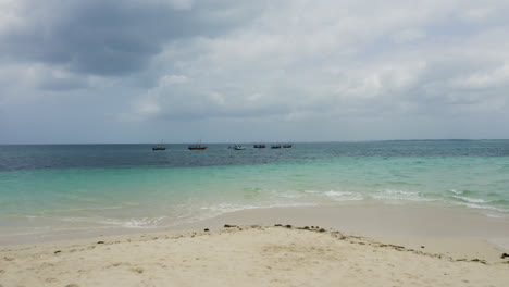 Pequeños-Botes-Anclados-En-La-Playa-De-Arena-Blanca-En-Alta-Mar-En-Zanzíbar,-Disparo-De-Drones