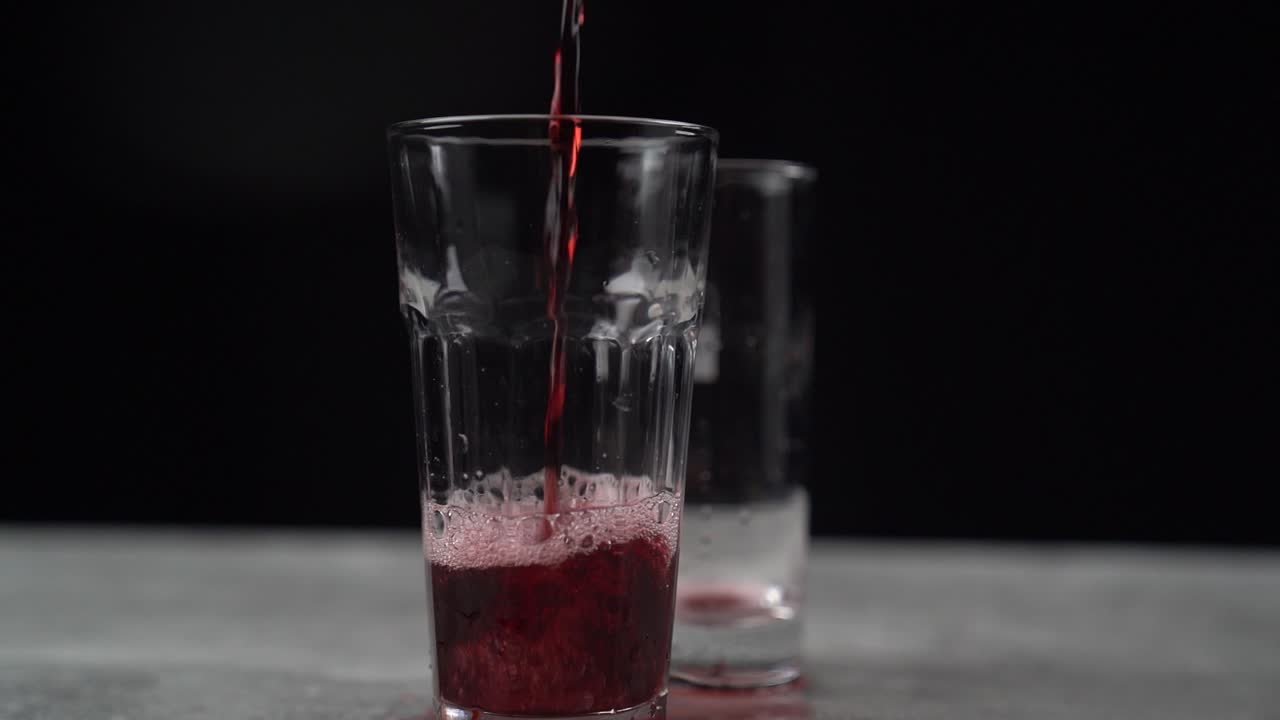Versamento e rovesciamento di bibita gassata rossa in due bicchieri.