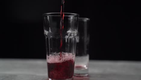 pouring and spilling red carbonated soda drink into two glasses