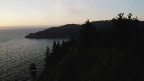 aerial view flying over forested hill on oregon coast, calm pacific ocean