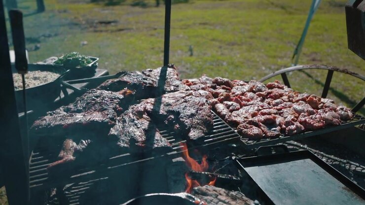 Grilled meat Asado, traditional Argentine barbecue with burning and smoking firewood, close up