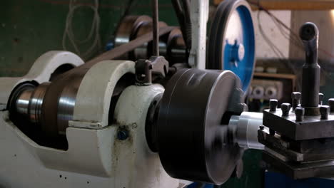 old lathe with spinning pulley and machining an aluminum piece leaving shaving long shot