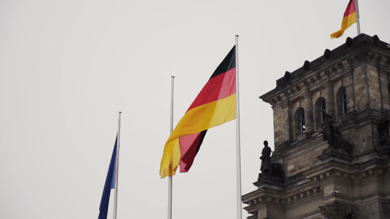 Bandiera Tricolore della Germania con Tre Bande Orizzontali Uguali nei Colori Nazionali Nero, Rosso e Oro, Sventola su Asta Accanto a Antica Torre Tedesca, Slow Motion a Mano Libera