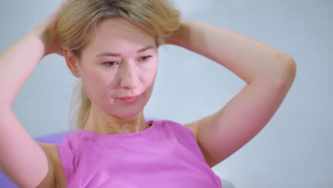 focused woman in pink sportswear performing core exercise with hands behind head on purple mat in a gym setting, maintaining concentration and effort in her fitness routine