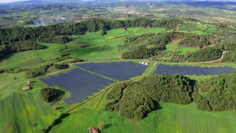 Aerial:-Panoramic-view-of-solar-panels-in-green,-grassy-field-on-a-sunny-day