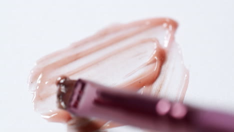 smudging some peach pink lip-moisturizing balm, with a brush applicator on a white sheet of paper