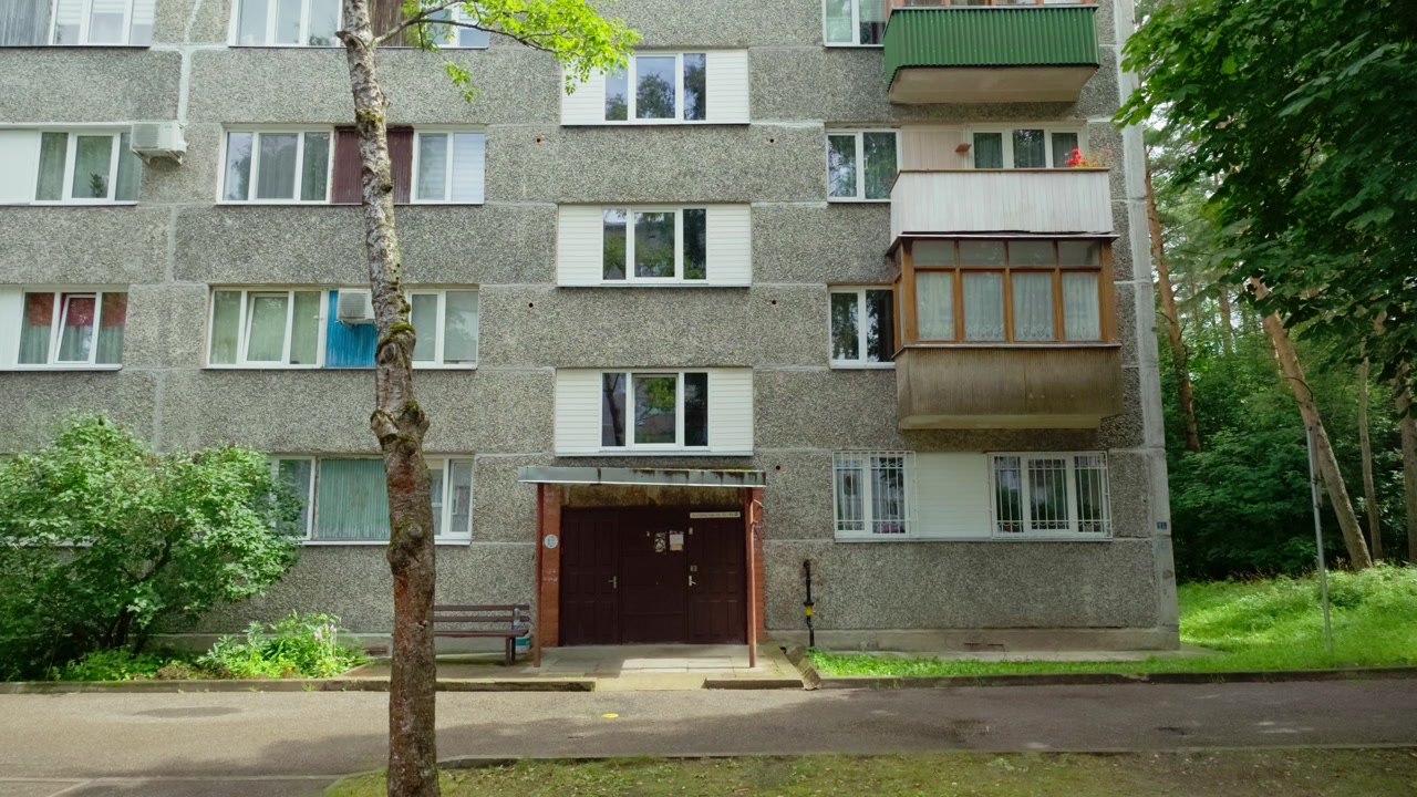Statisk vidvinkelbilde som viser fasaden til et betongbygg med flere etasjer, balkonger og hovedinngang i et fredelig nabolag i Daugavpils, Latgale, Latvia