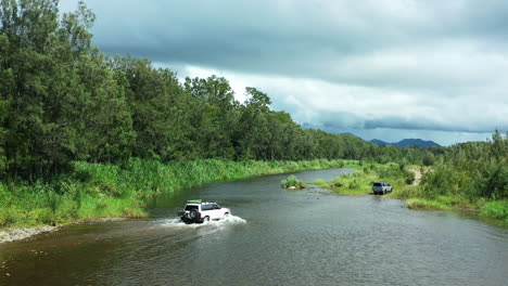 Aerial-4K-Drone-Of-Four-Wheel-Drive-Vehicles-Crossing-Flowing-Creek-On-Stormy-Day-In-Australia