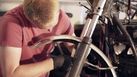 close up of young blonde man loosening nut with wrench during motorcycle teardown