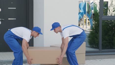 Two young workers of removal company are loading boxes and furniture into a minibus