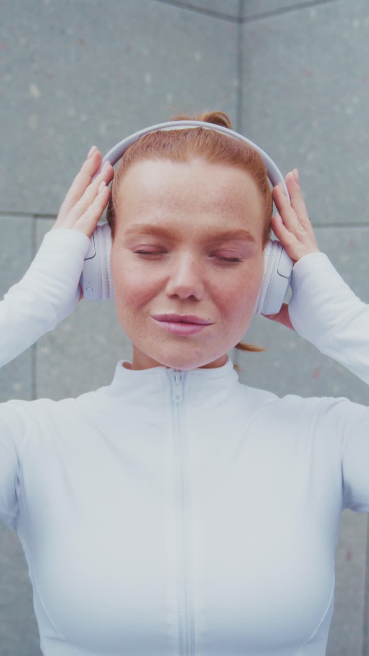 Una giovane donna sicura di sé mostra le sue cuffie alla moda, emanando un senso di empowerment e concentrazione in un ambiente urbano moderno, evidenziando una fusione di moda e tecnologia