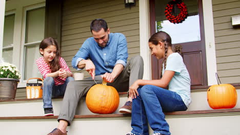 father and daughters carving halloween pumpkin on house steps
