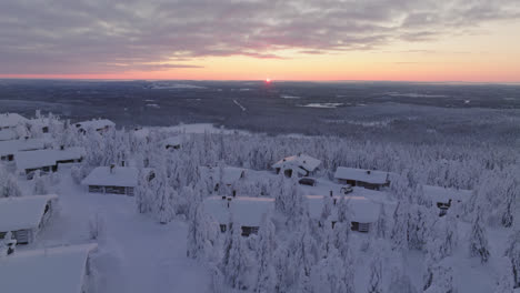 aerial view backwards over snowy mountain cabins, winter morning in lapland