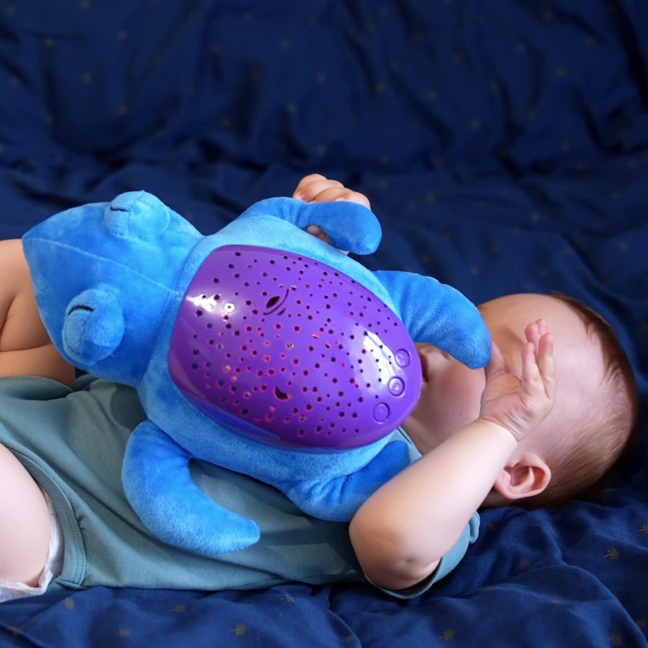 Little infant baby boy lies holding a toy. Healthy child playing with big blue soft turtle. Blue backdrop