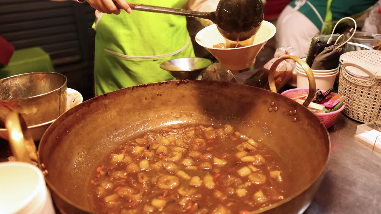 Vendor ladles hot fish maw soup at vibrant Bangkok street food stall under warm lighting