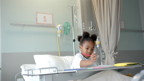 Niña-Afroamericana-Dibujando-En-Un-Cuaderno-En-La-Cama-De-Un-Hospital,-En-Cámara-Lenta