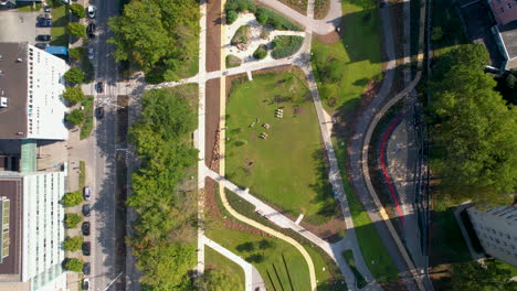 aerial top down shot of green park with path and driving cars in road in gdynia city at sunny day