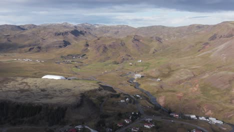 Sun-shining-on-highlands-behind-Hveragerði-village-in-Iceland,-scenic-valley,-aerial