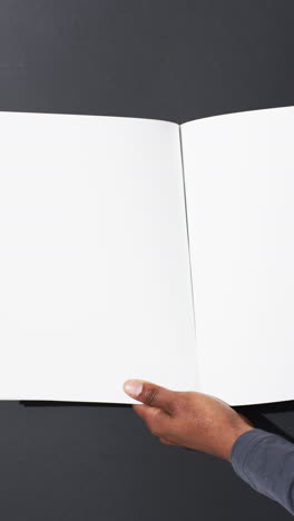 vertical video of hand of african american man with book with white blank pages on grey background