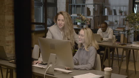 two female employees looking something at computer and talking together in the office