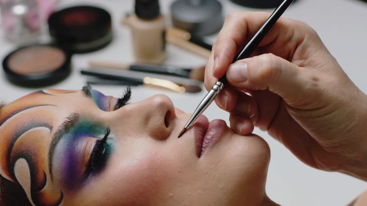 Make-up artist che avvicina un pennello sottile e applica tratti precisi per definire le labbra alla toletta, con i suoi strumenti.