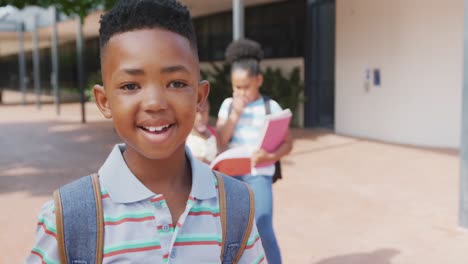 Video-portrait-of-smiling-african-american-schoolboy-with-schoolbag-outside-school,-with-copy-space