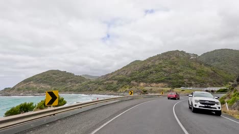 cars travel a coastal road with ocean views and lush hills under cloudy skies, capturing the essence of a scenic journey