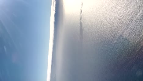 Vertical-aerial-footage-of-blue-sky-over-the-sea-with-a-huge-reflection-in-the-water