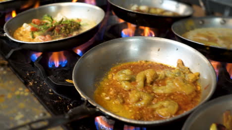 sartenes de acero inoxidable abarrotan una estufa comercial en una cocina, varios platos de menú hierven a fuego lento sobre llamas en un restaurante indio, deslizador de cámara lenta hd
