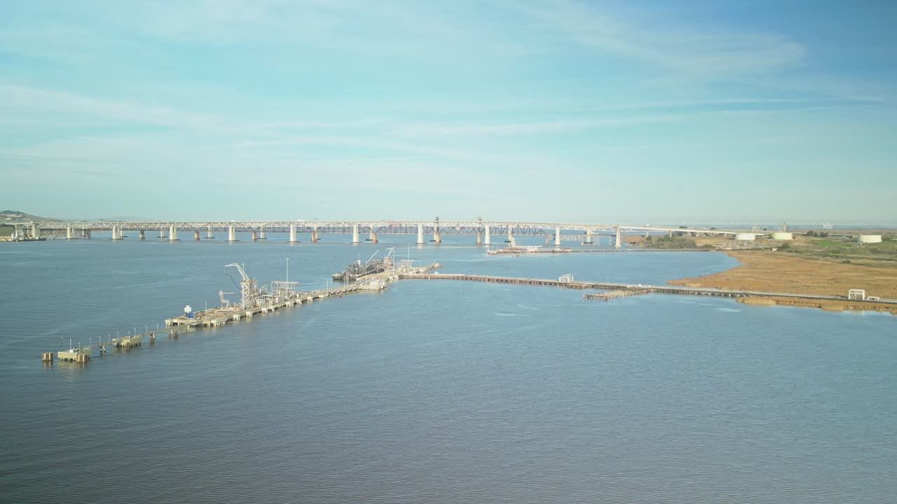 Aerial tracking left of wetlands and shoreline in Martinez, California, with hills and open space, George Miller Jr. Memorial bridge connects towns