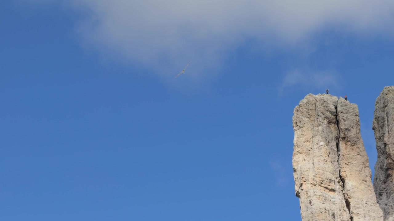 Vista distante di un aliante bianco che plana attraverso un vasto cielo azzurro e limpido sopra le Torri del Vajolet, Dolomiti. Italia. Spazio per il testo.